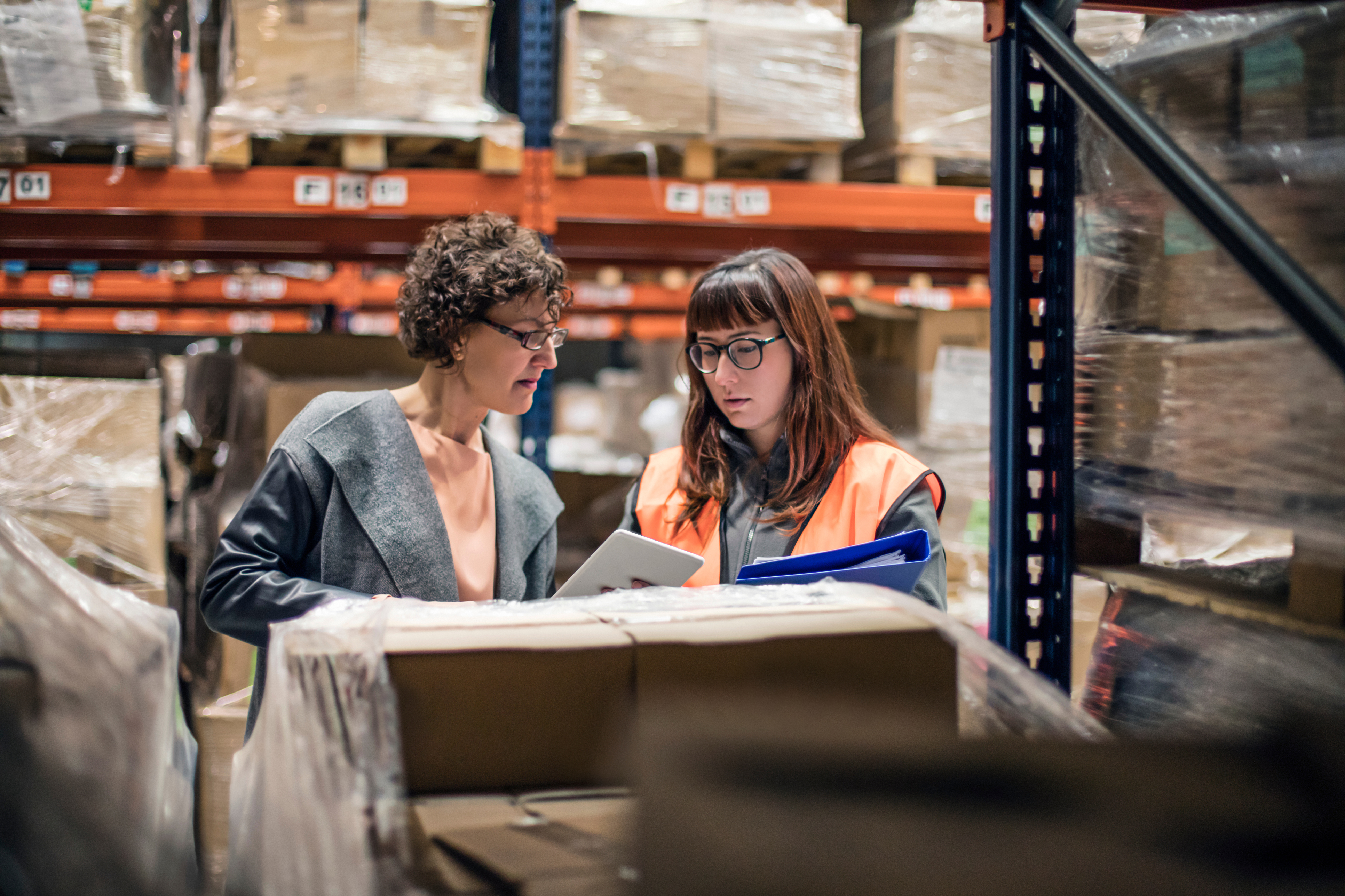 Woman with digital tablet in warehouse talking to worker in the aisle.